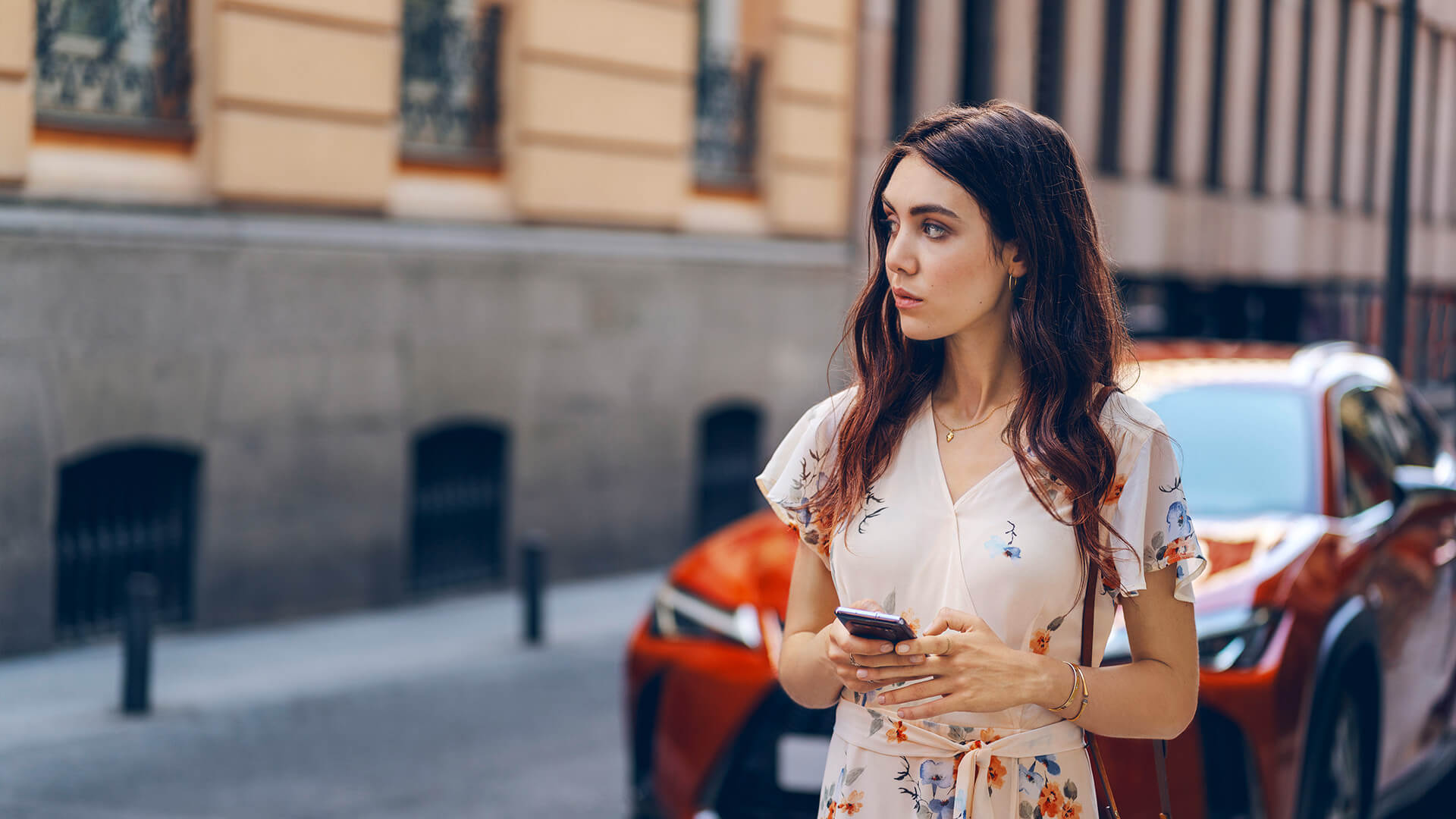 Junge Frau mit Smartphone vor Lexus UX Hybrid